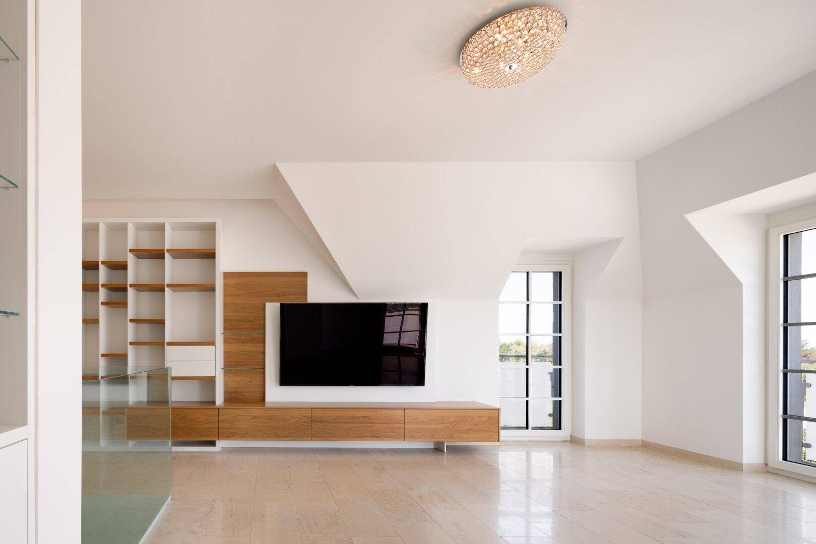 Geräumiger Wohnbereich im Dachgeschoss mit Dachschrägen, Holzelementen und großem Fenster, hell und modern.