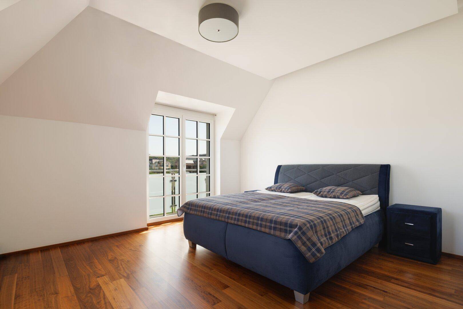 Gemütliches Schlafzimmer im Dachgeschoss mit Holzboden und großem Fenster, bietet eine ruhige Rückzugsmöglichkeit.