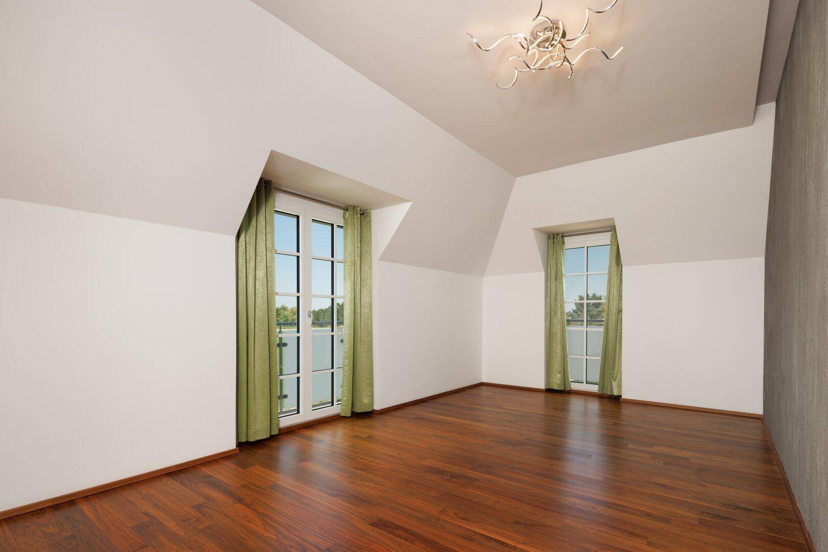 Helles Schlafzimmer im Dachgeschoss mit Holzboden und großen Fenstern, bietet viel Tageslicht.