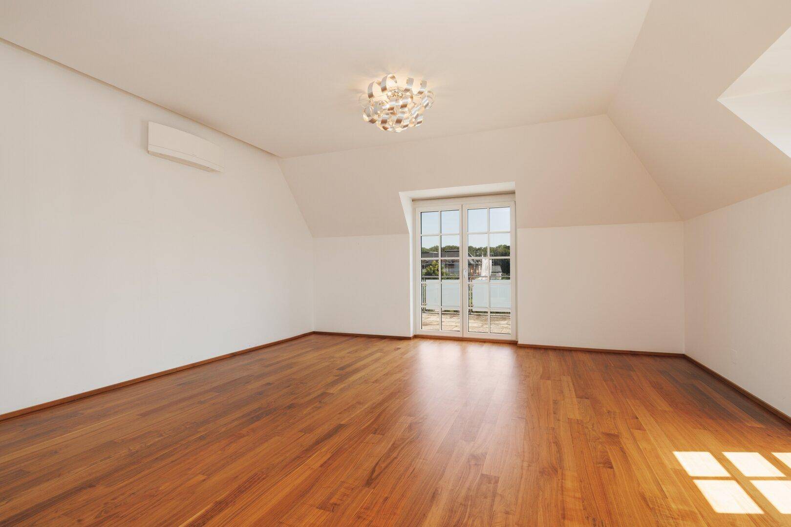 Helles Schlafzimmer im Dachgeschoss mit Holzboden und Zugang zum luxuriösen Badezimmer.