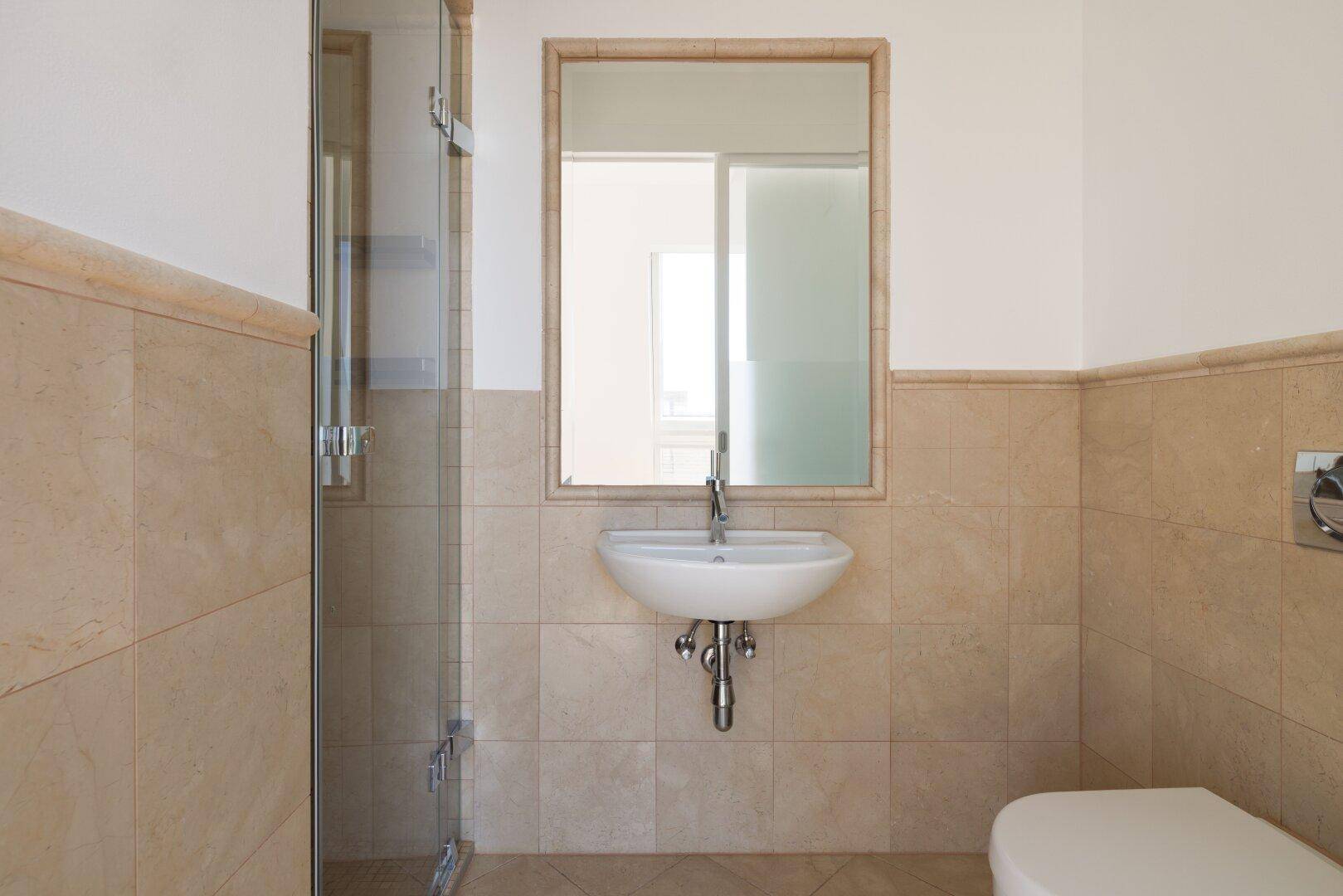 Modernes Badezimmer mit beigen Fliesen, elegantem Waschbecken und großem Spiegel.
