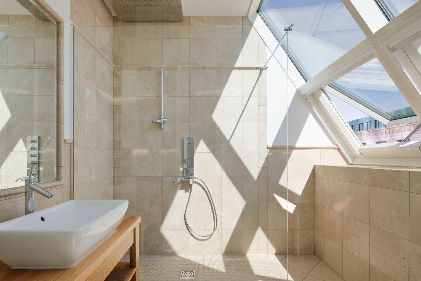 Modernes Badezimmer mit begehbarer Dusche, beigen Fliesen und viel Tageslicht durch Dachfenster.
