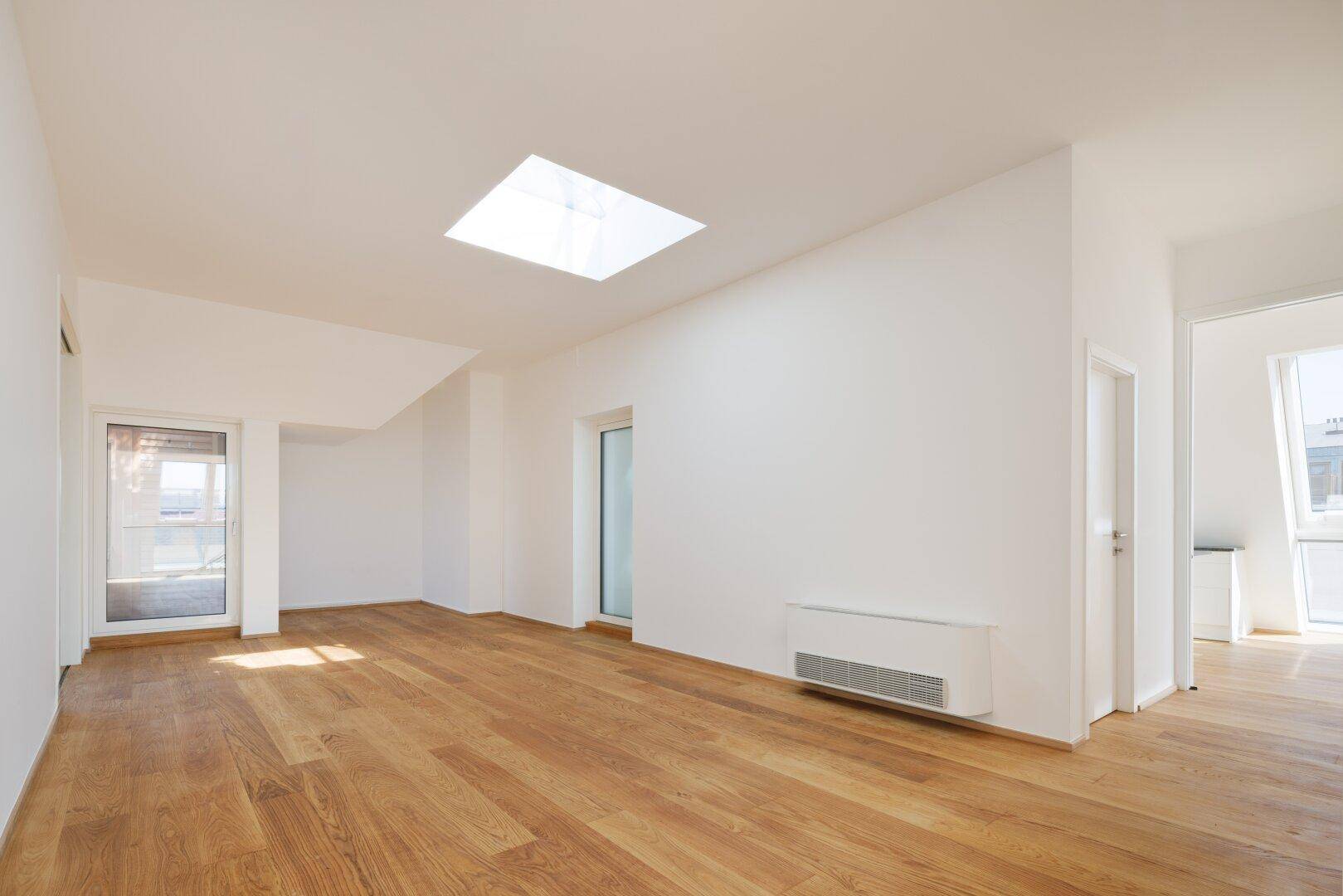 Geräumiger, heller Raum mit Holzboden und einem großen Oberlicht, das viel Tageslicht spendet.