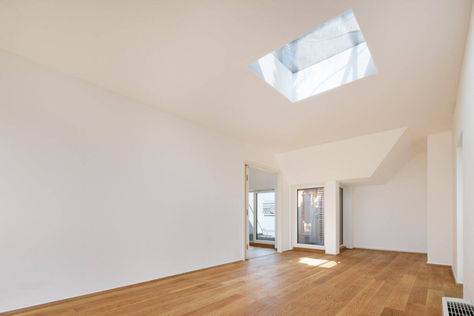Großer, lichtdurchfluteter Raum mit Holzboden und einem zentralen Oberlicht, ideal für flexible Nutzung.