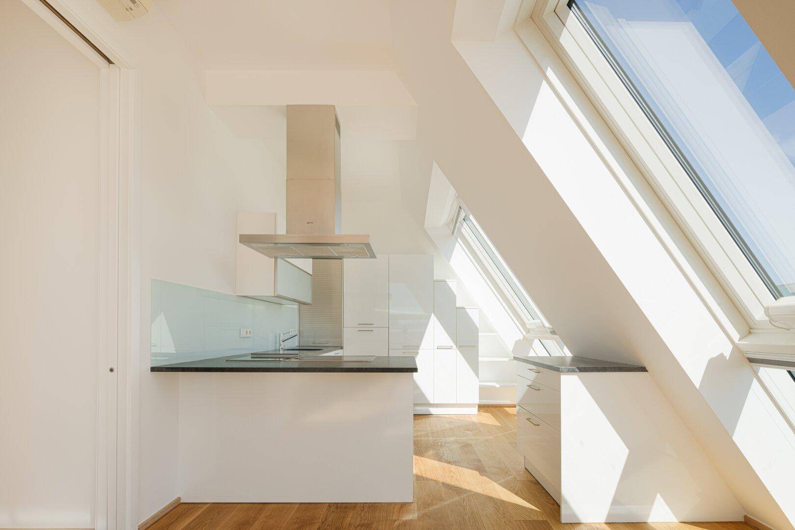 Moderne Küche mit weißen Schränken, Dunstabzugshaube und viel Tageslicht durch Dachfenster.