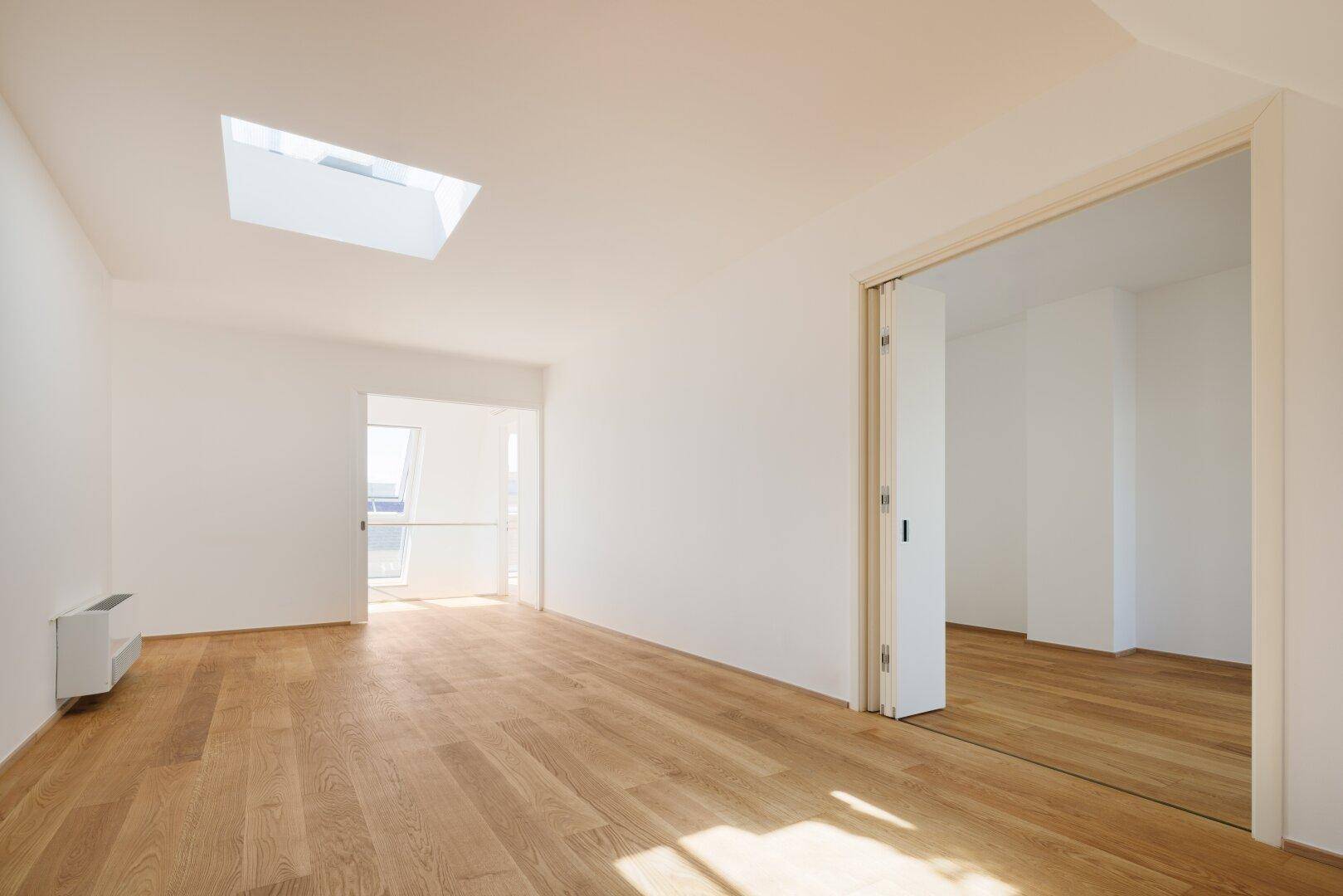 Heller, geräumiger Raum mit Holzboden und Oberlicht, der Zugang zu weiteren Zimmern bietet.