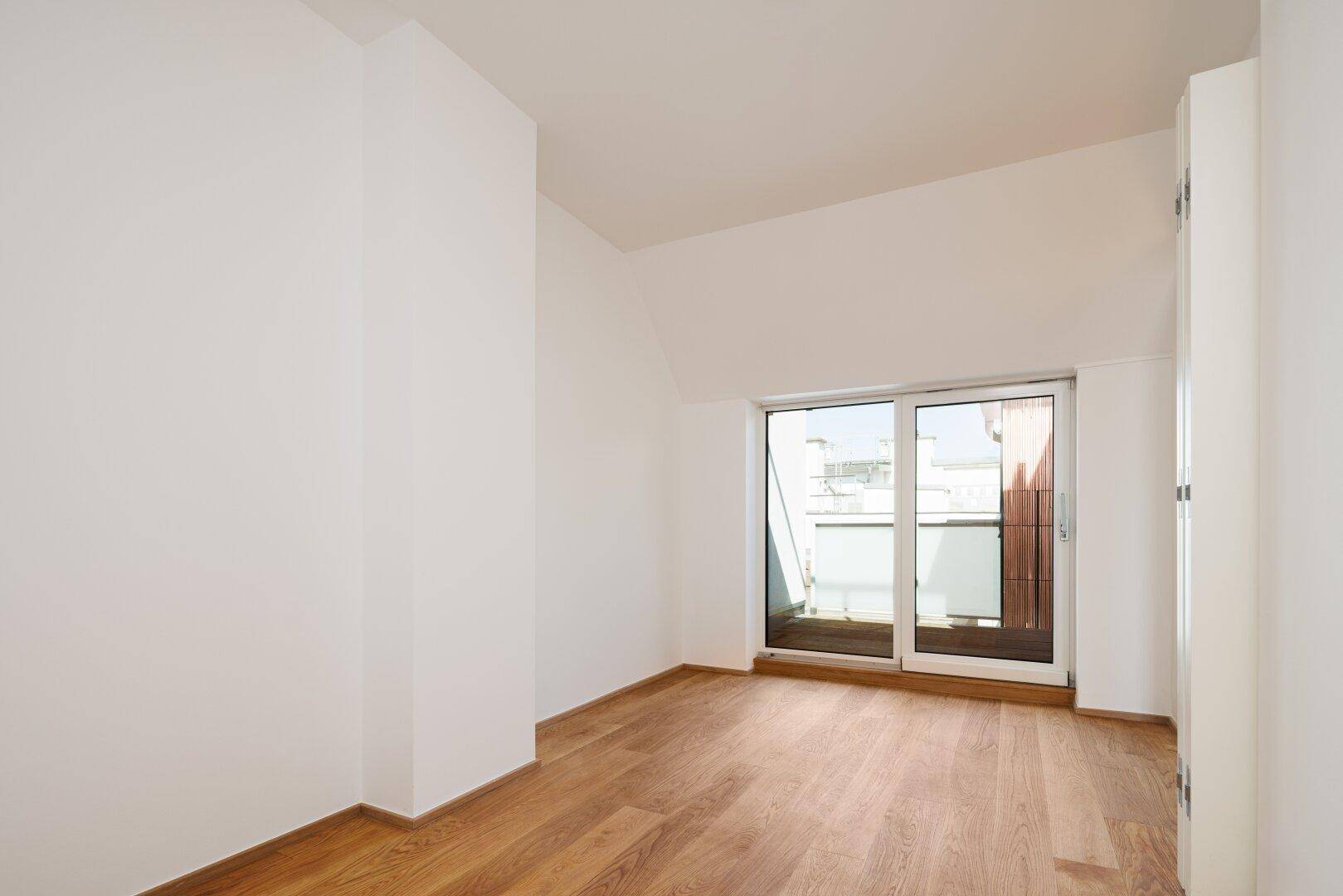 Helles Zimmer mit Holzboden und Zugang zu einem Balkon oder einer kleinen Terrasse.