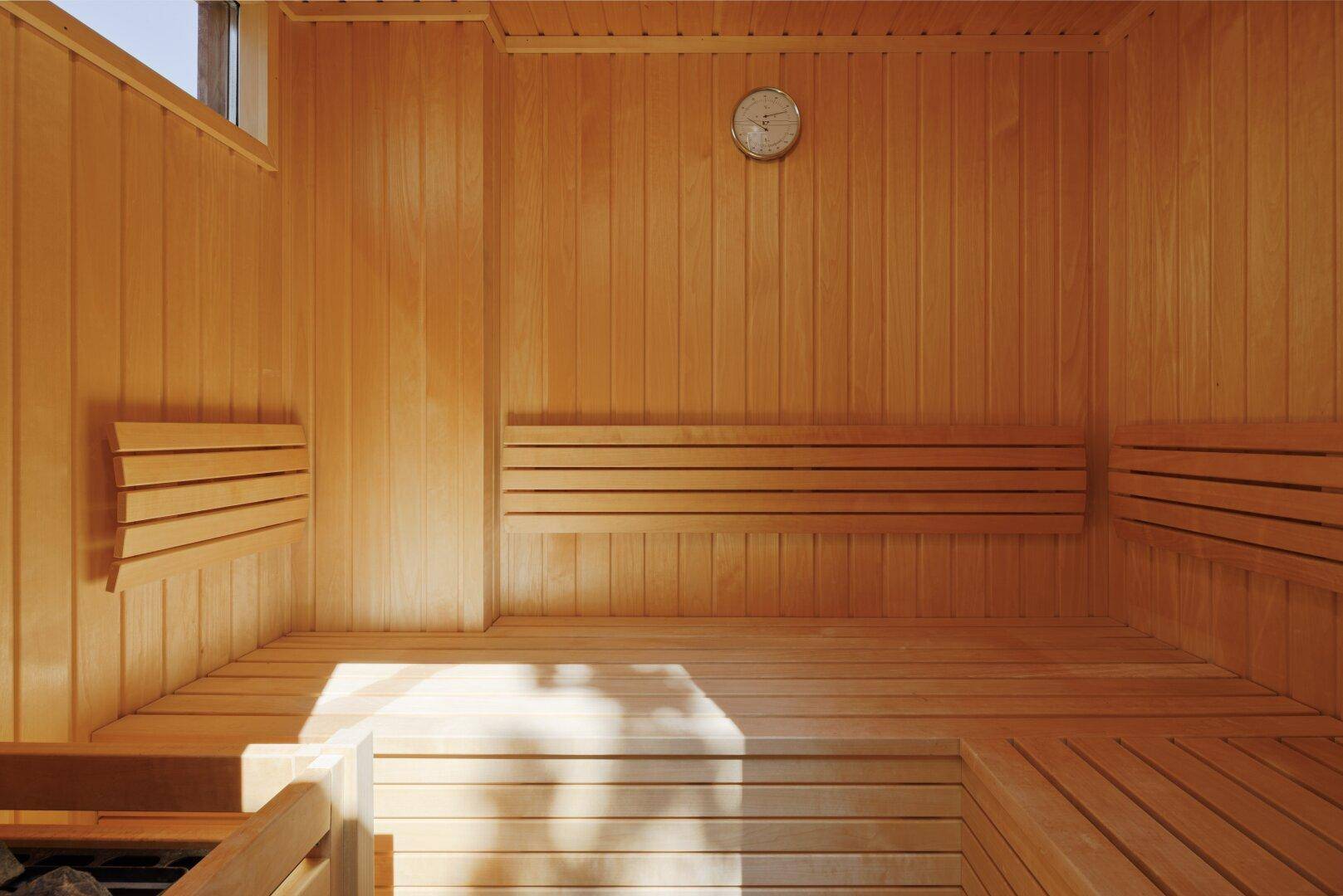 Gemütlicher Saunaraum aus hellem Holz mit Bänken und einem Thermometer, bereit zur Entspannung.