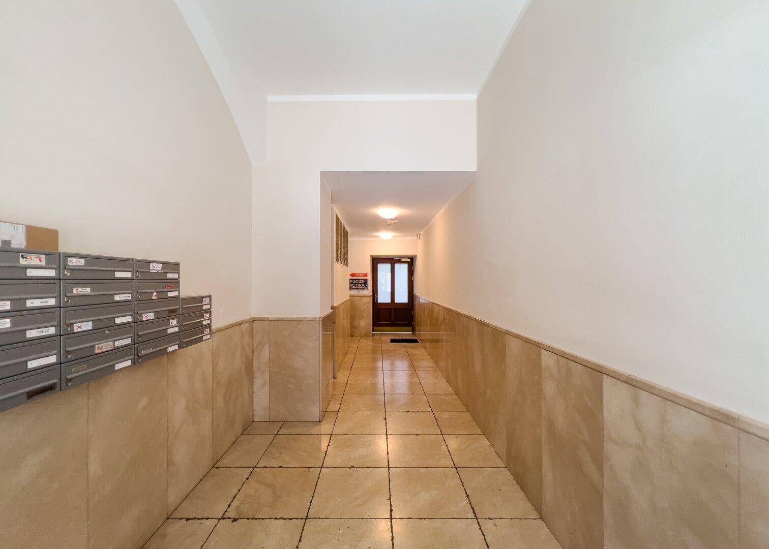 Eingangsbereich mit Fliesenboden, Briefkästen und Zugang zu einem Treppenhaus und Aufzug.