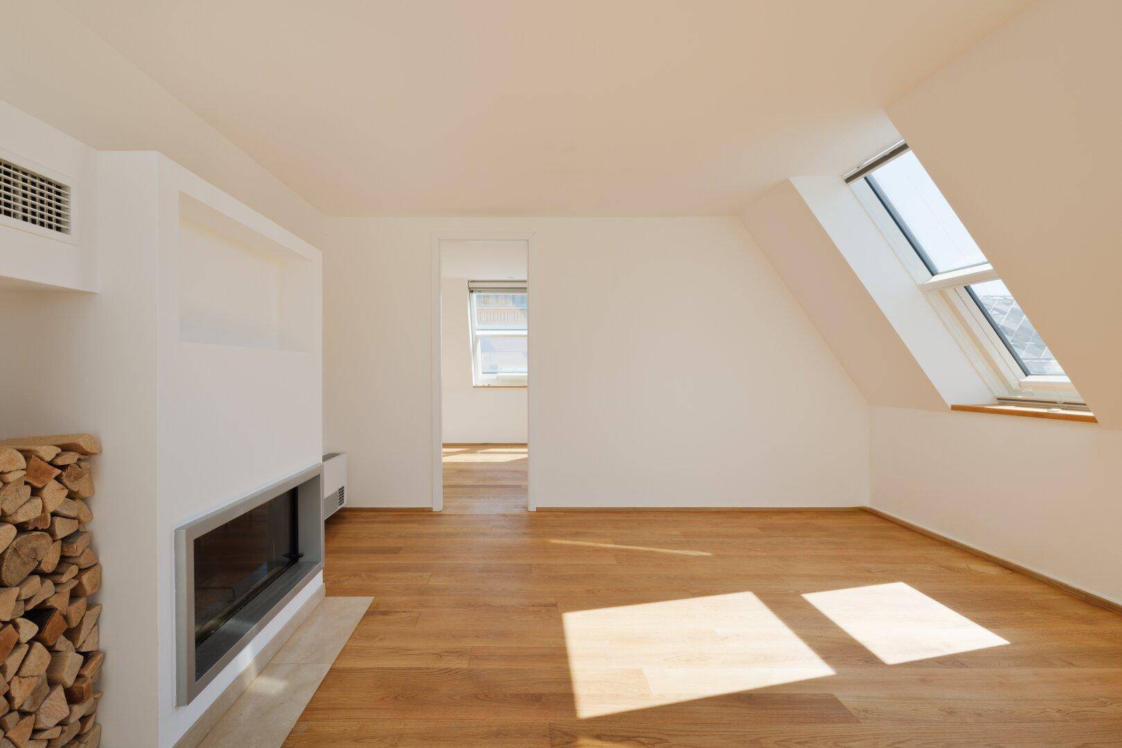 Heller Wohnbereich mit Holzboden, modernem Kamin und schrägen Dachfenstern, die viel Licht hereinlassen.
