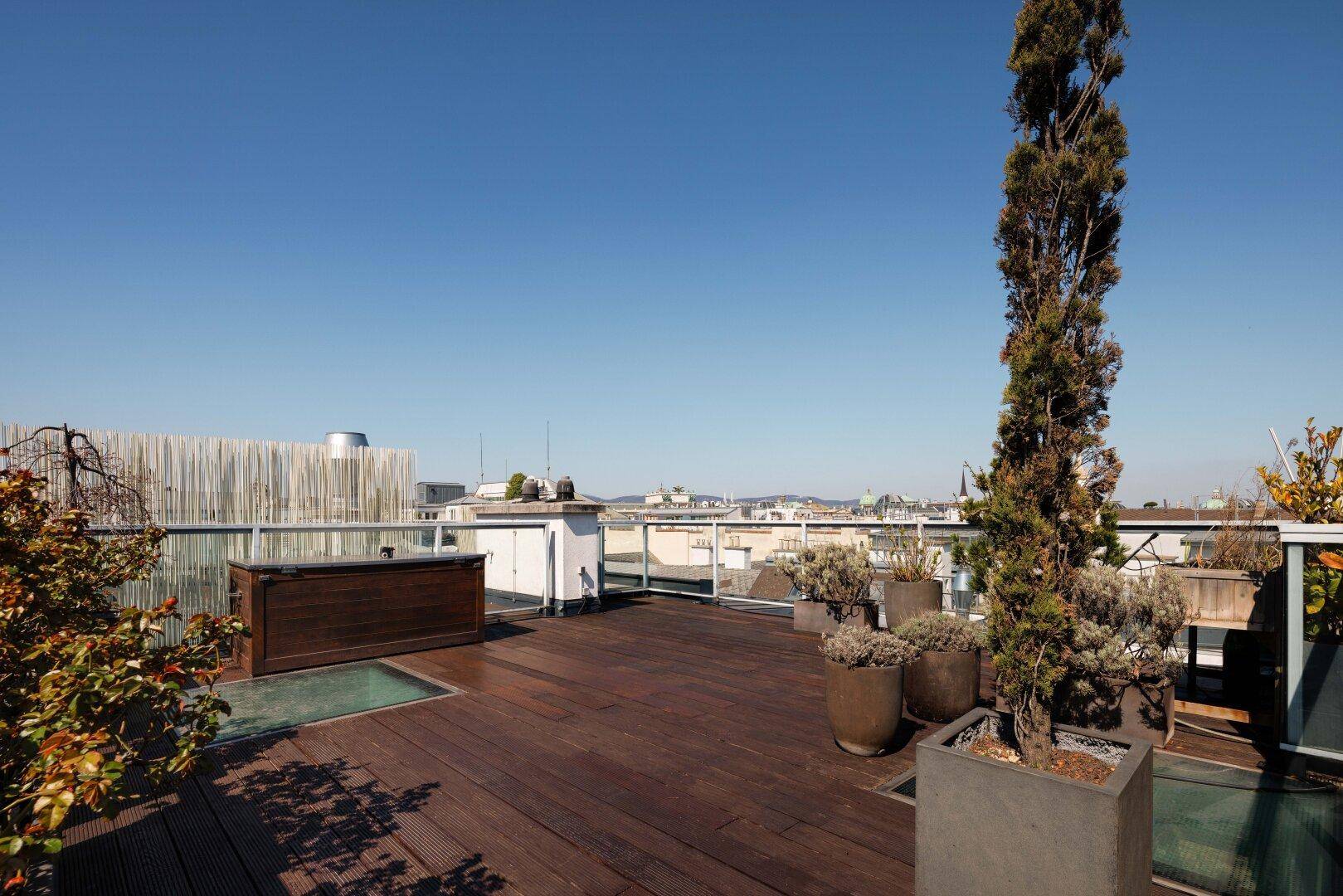 Weitläufige Dachterrasse mit Holzboden, Pflanzen und Panoramablick über die Stadt.