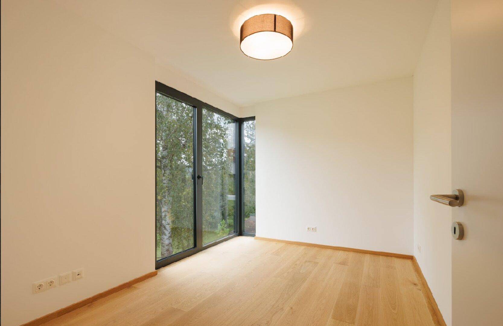 Heller, leerer Raum mit Holzboden und großen Eckfenstern, die viel Tageslicht hereinlassen.