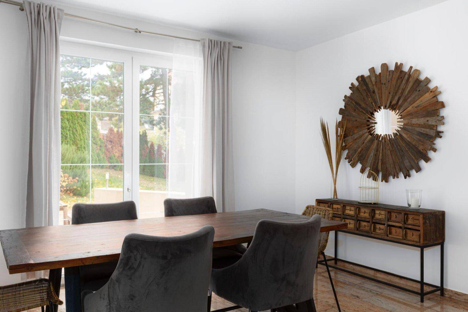 Essbereich mit Holztisch, modernen Stühlen und dekorativem Spiegel, mit Blick in den Garten.