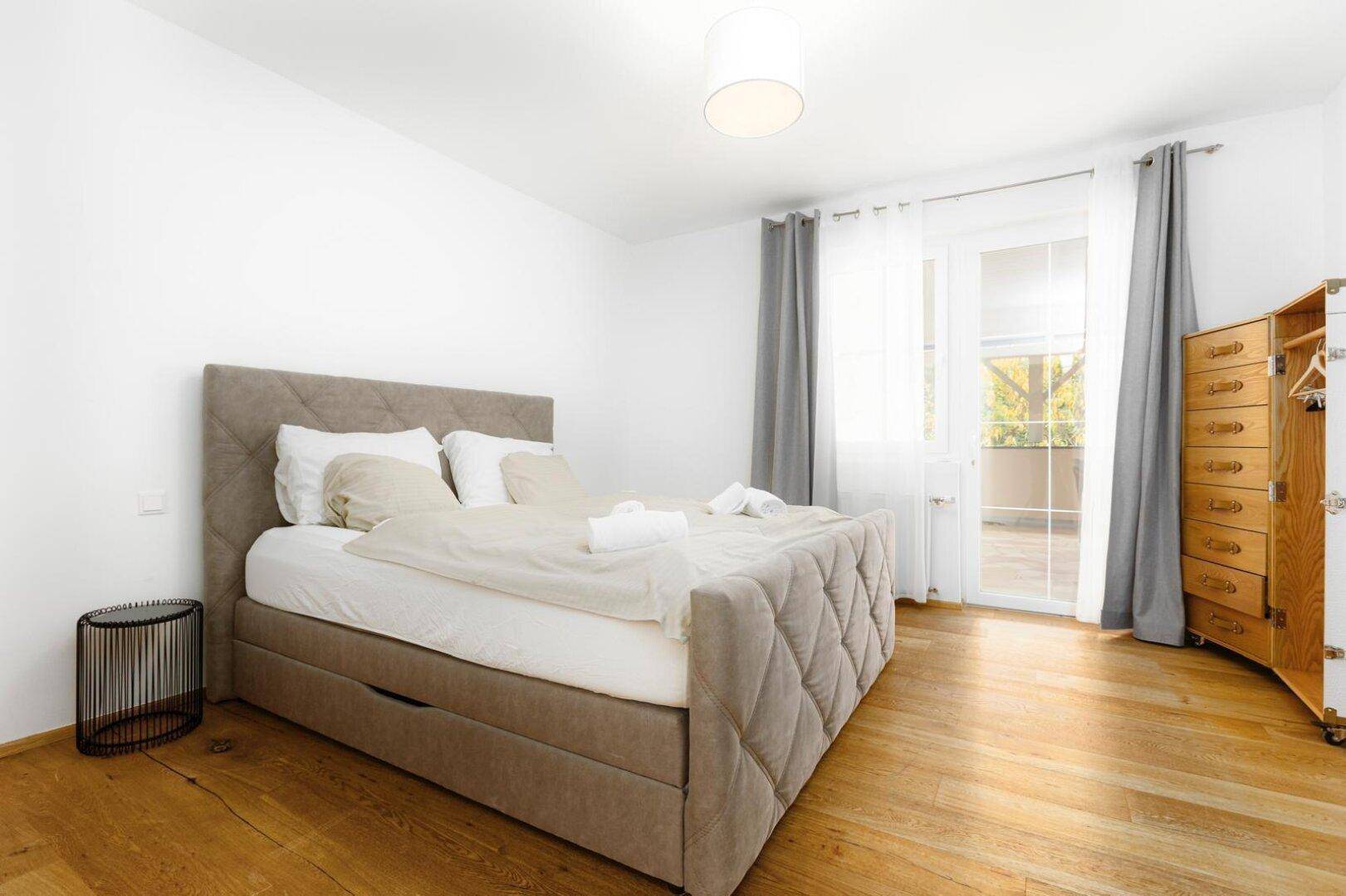 Geräumiges Schlafzimmer mit Doppelbett, Holzboden und Zugang zu einem Balkon.