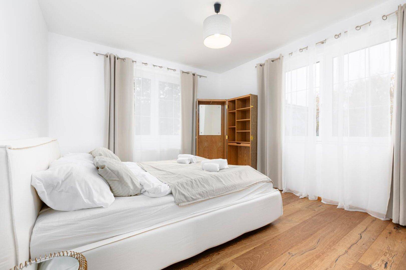 Helles Schlafzimmer mit Doppelbett, Holzboden und großen Fenstern, modern eingerichtet.