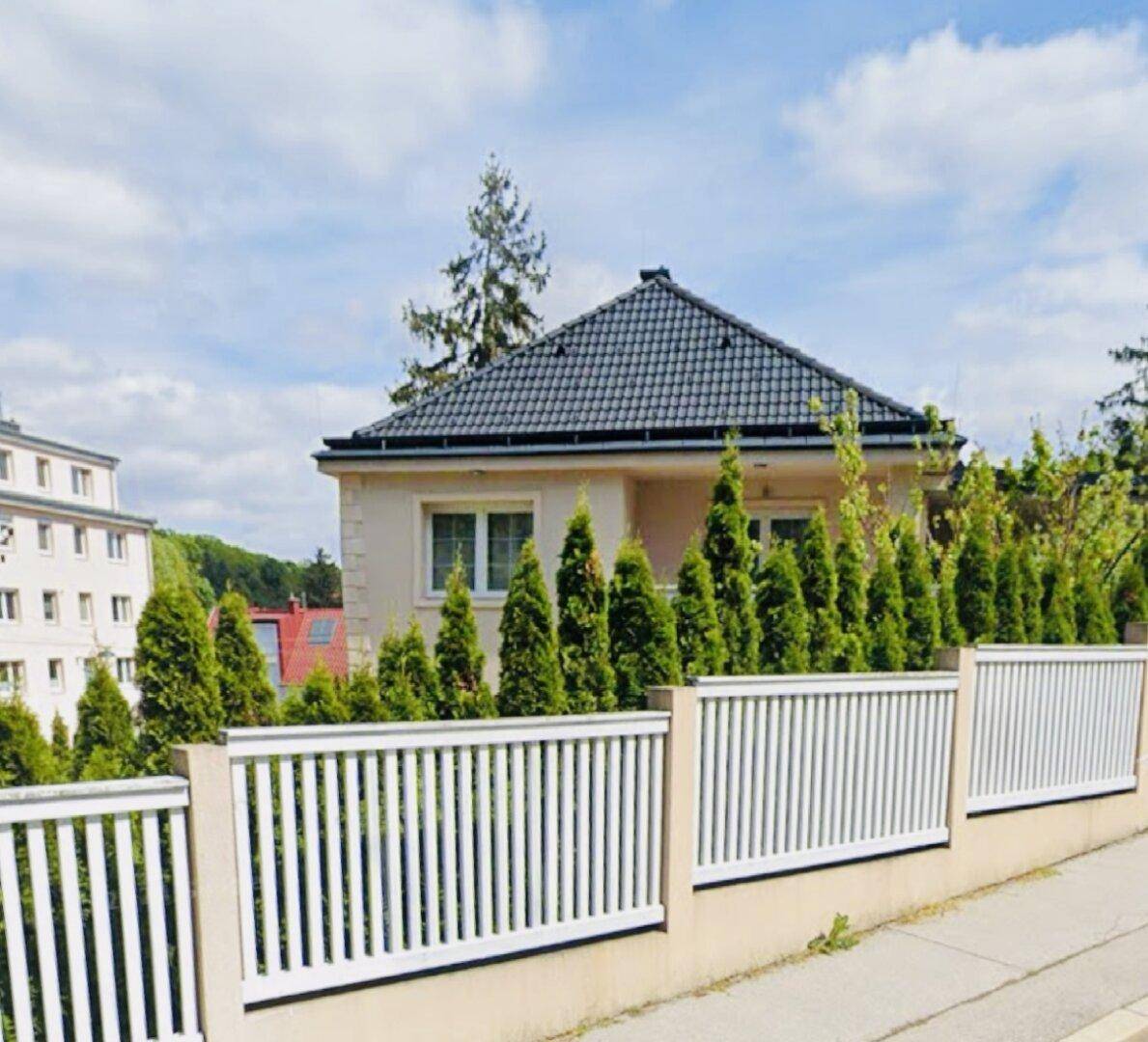 Freistehendes Haus mit gepflegtem Vorgarten und weißem Zaun unter blauem Himmel.