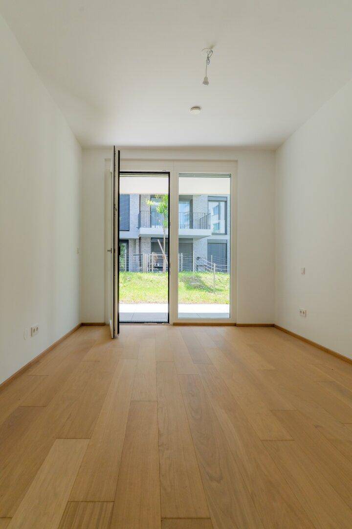 Heller, leerer Raum mit Holzboden und Zugang zu einer Grünfläche im Außenbereich.