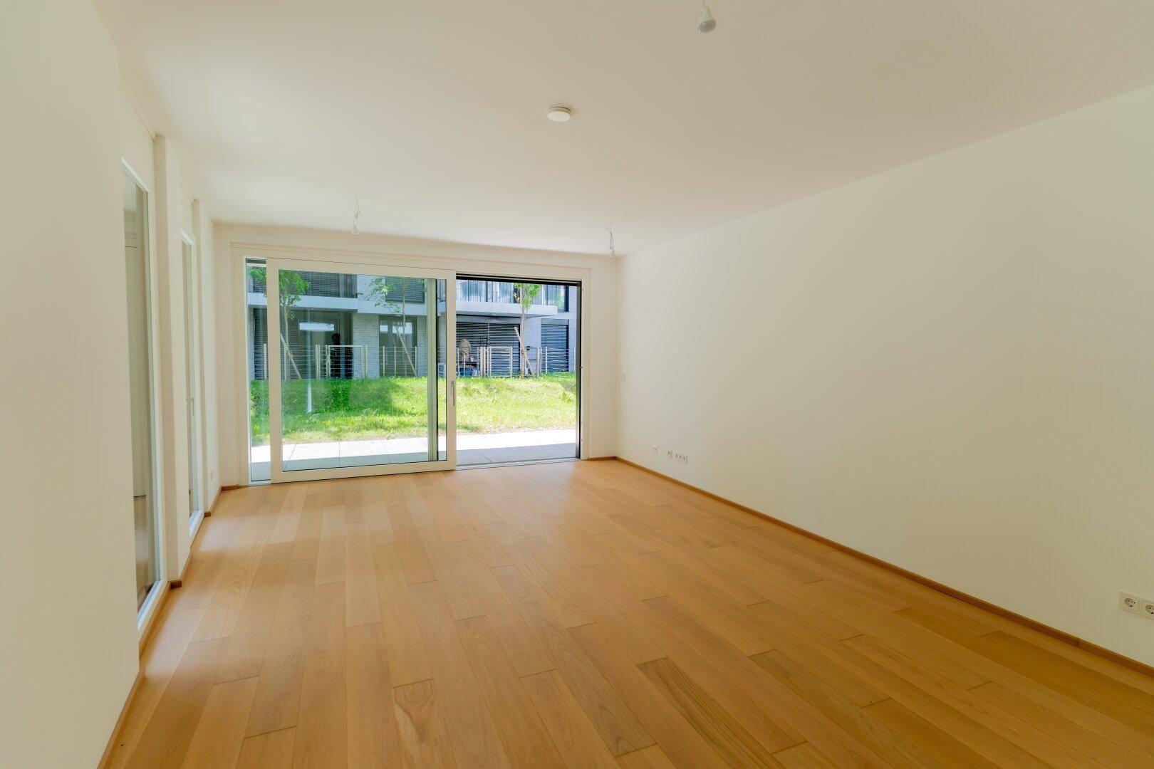 Lichtdurchfluteter Raum mit Parkettboden und großen Schiebetüren, die zum Garten führen.