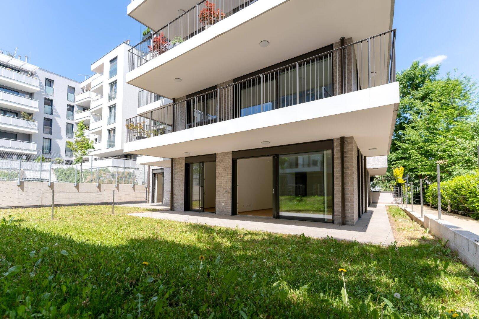 Modernes Wohngebäude mit Terrassen und Balkonen, umgeben von gepflegten Grünflächen.