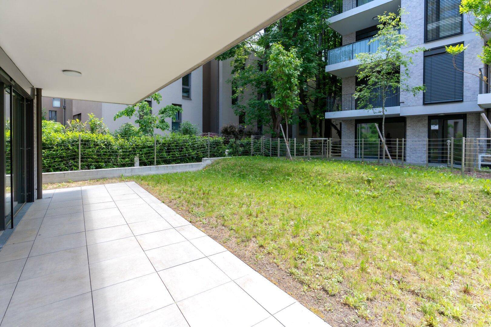 Großzügige Terrasse mit angrenzender Rasenfläche und Blick auf die moderne Wohnanlage.