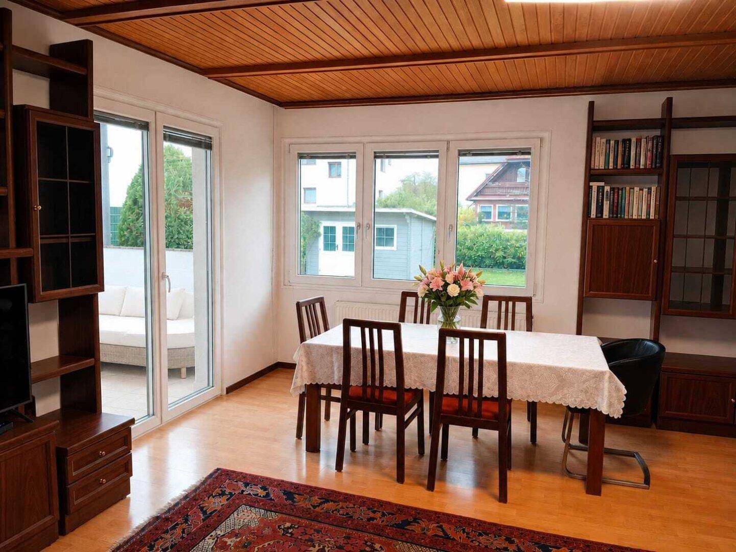 Esszimmer mit Holztäfelung an der Decke, großem Esstisch und Zugang zur Terrasse.