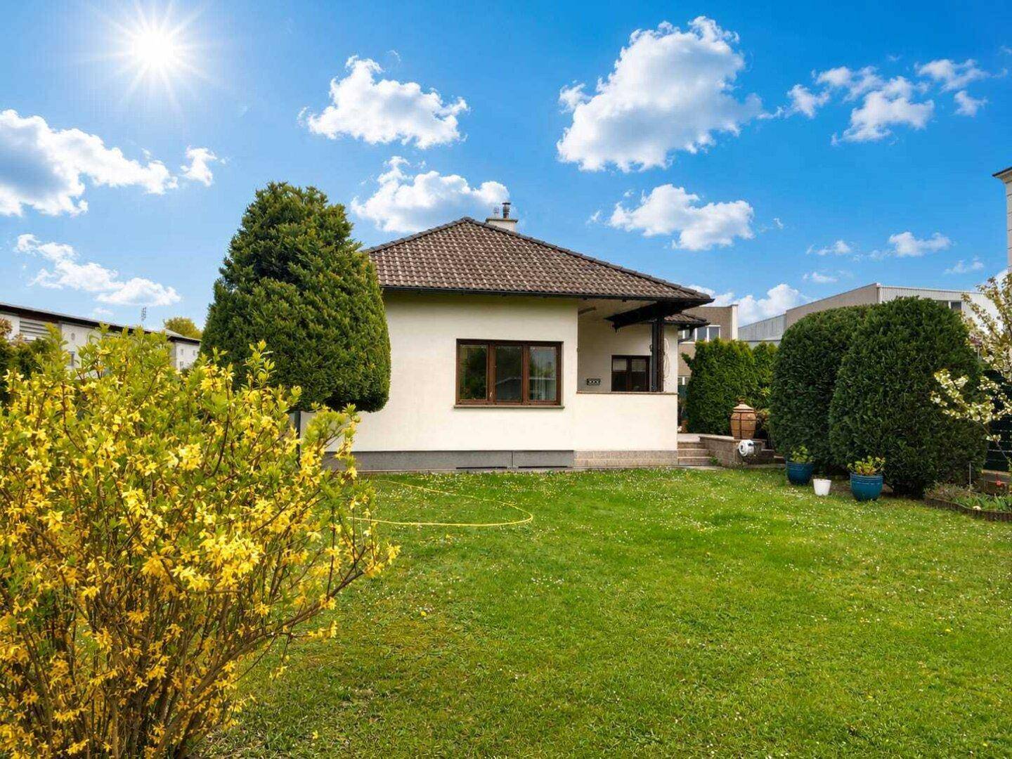 Freistehendes Einfamilienhaus mit gepflegtem Rasen und blühenden Sträuchern unter blauem Himmel.