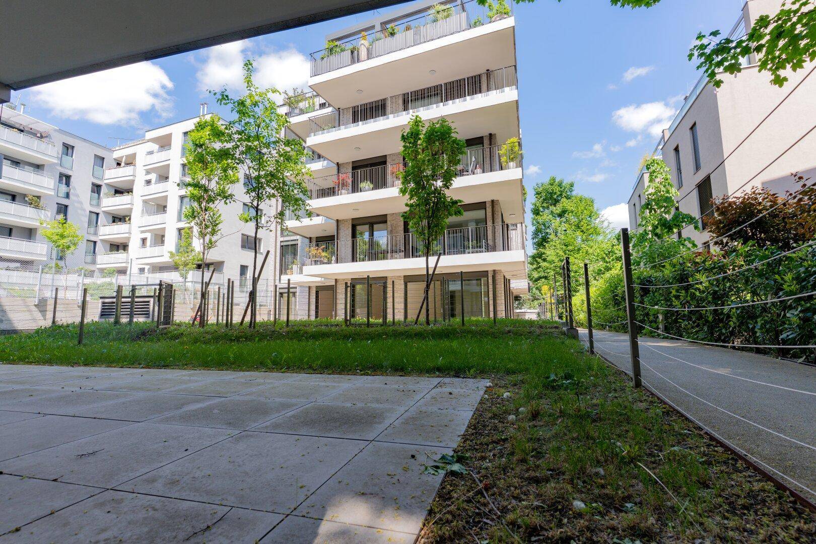 Ansicht eines modernen Mehrfamilienhauses mit mehreren Balkonen und Dachterrasse in grüner Umgebung.