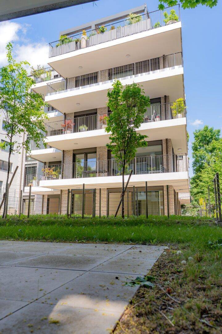 Modernes Wohngebäude mit gestuften Balkonen und einer Dachterrasse unter blauem Himmel.