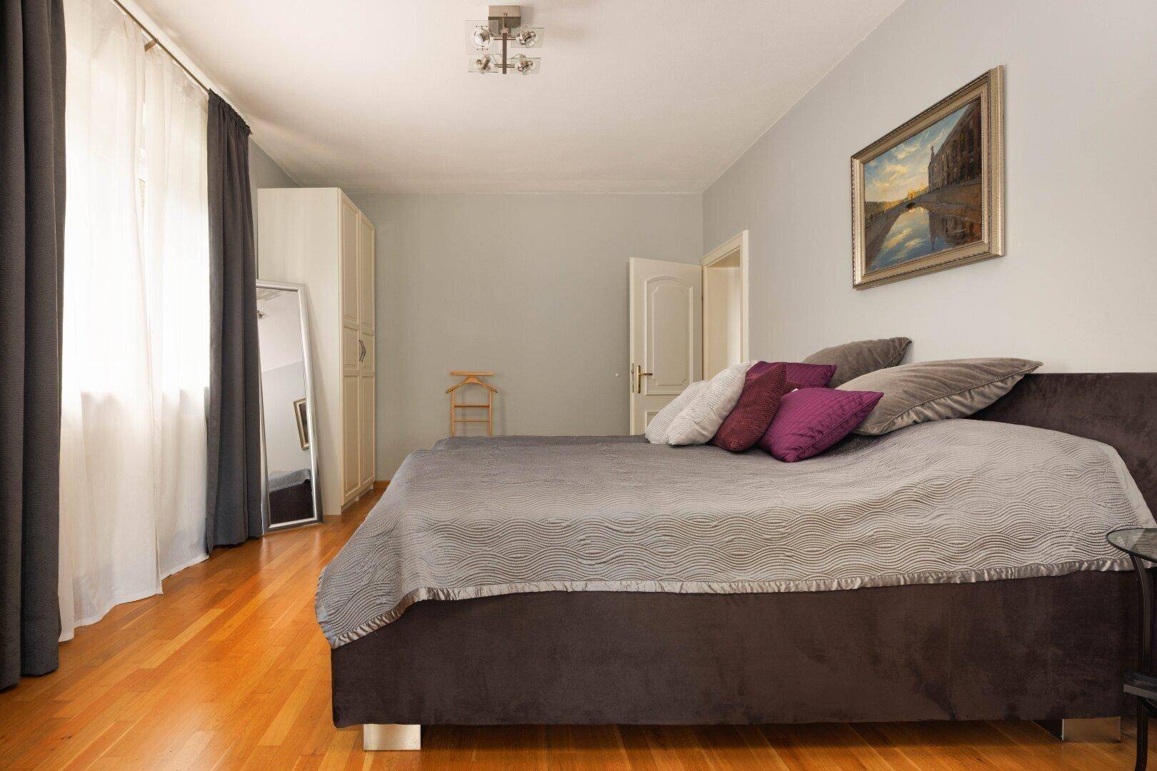 Gemütliches Schlafzimmer mit Holzboden, großem Bett und schlichten Vorhängen.