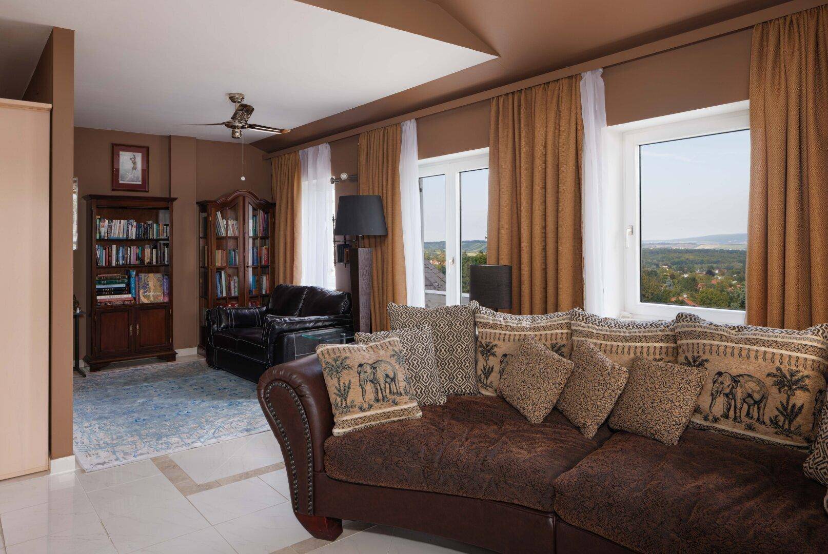 Gemütliches Wohnzimmer mit braunen Sofas, Bücherregal und weitem Blick in die Landschaft.