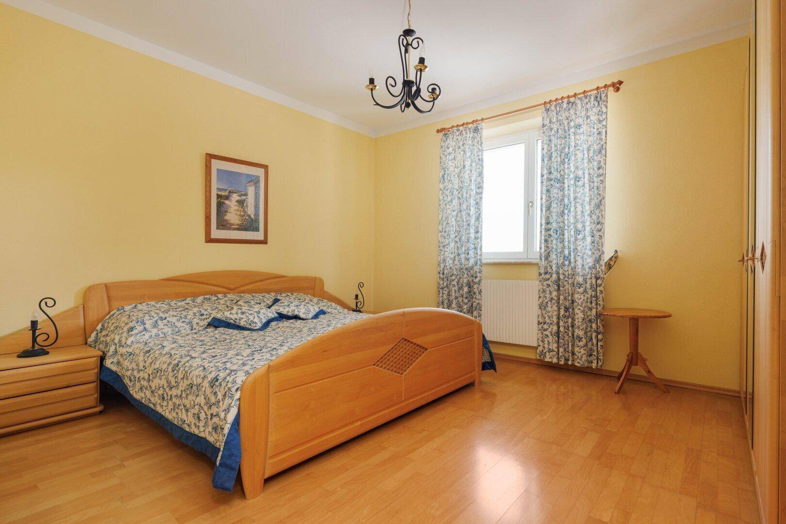 Helles Schlafzimmer mit gelben Wänden, Holzboden und klassischem Doppelbett.