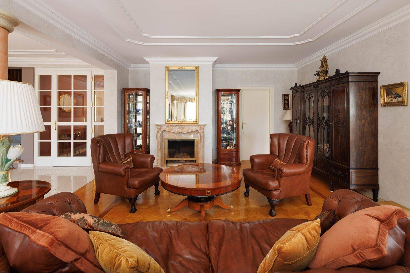 Elegantes Wohnzimmer mit Kamin, Stuckdecke und klassischen Ledermöbeln.