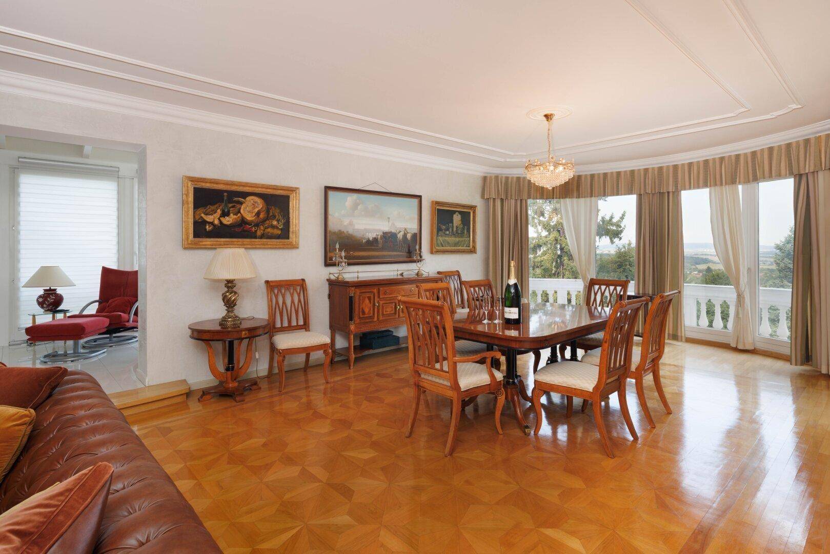Eleganter Essbereich mit Parkettboden, großem Esstisch und Zugang zu einem Balkon.