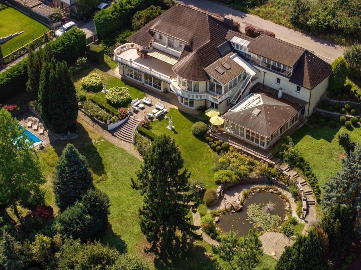 Luftaufnahme der weitläufigen Villa mit großem Garten, Poolbereich und Teichanlage in grüner Umgebung.