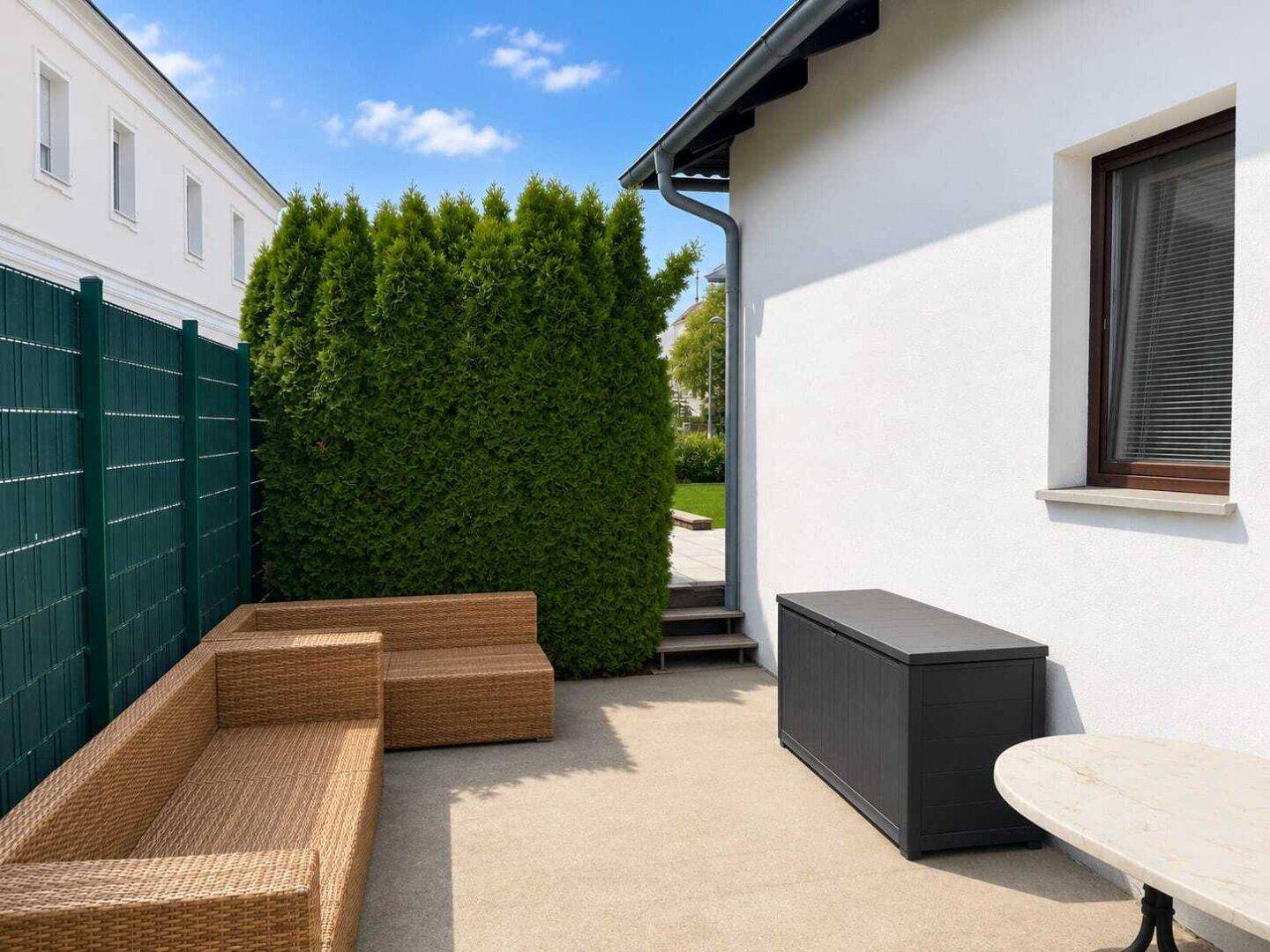 Gemütlicher Außenbereich mit Korbmöbeln, einer hohen Hecke und einem Gartenschrank.