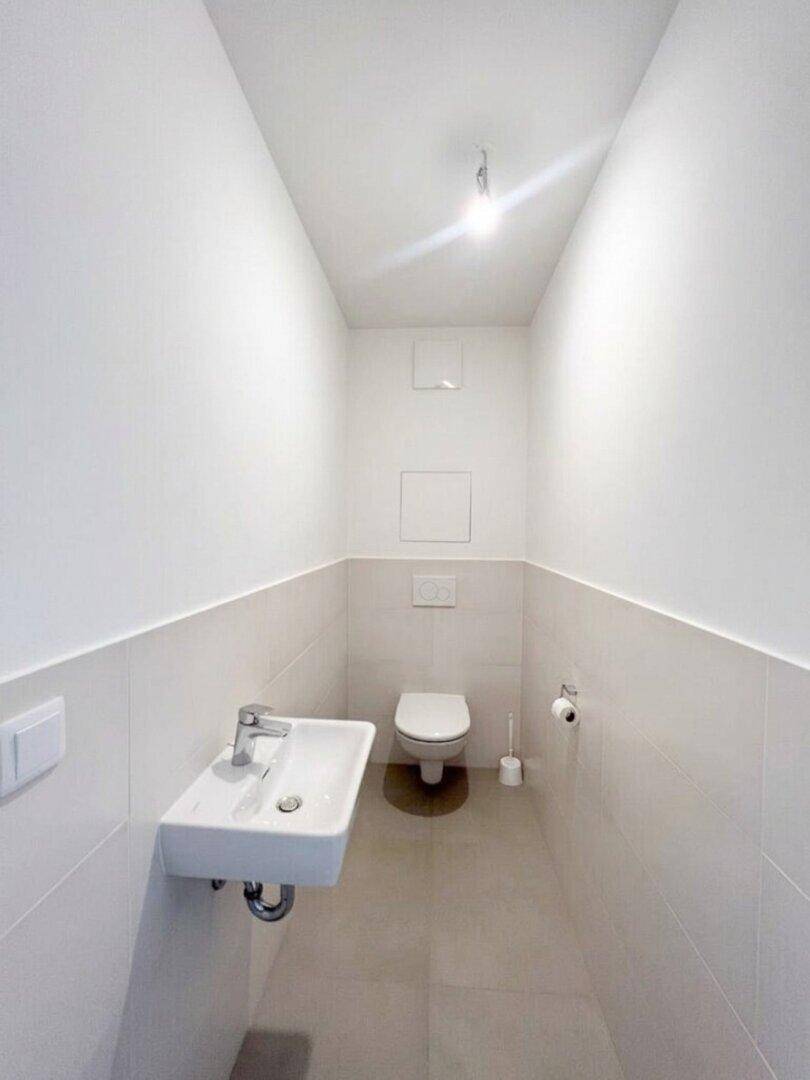 Modernes Gäste-WC mit wandhängender Toilette und kleinem Waschbecken, hell gefliest.