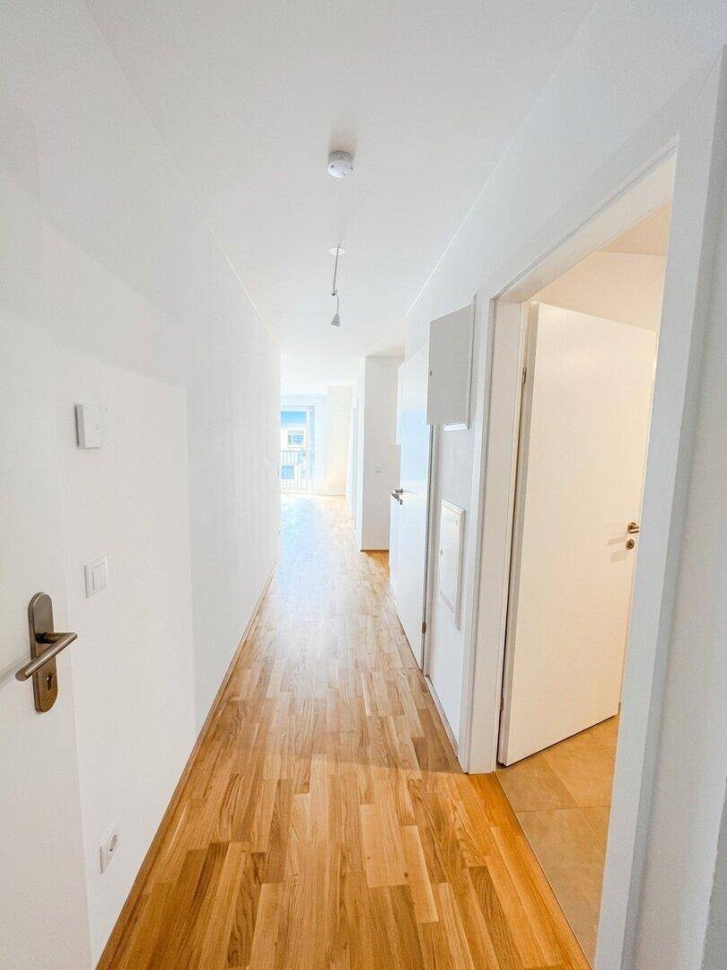 Langer, heller Flur mit Holzboden und mehreren Türen, der verschiedene Räume verbindet.