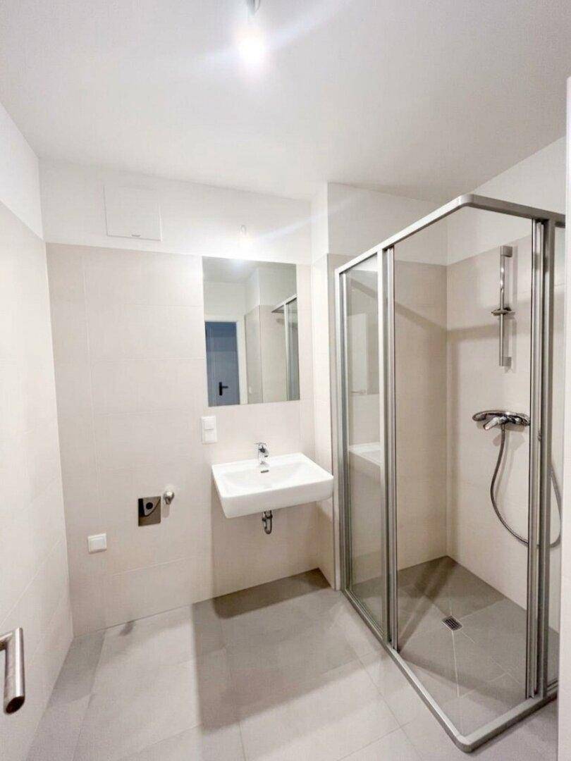 Helles Badezimmer mit Duschkabine, Waschbecken und Spiegel, modern gefliest.