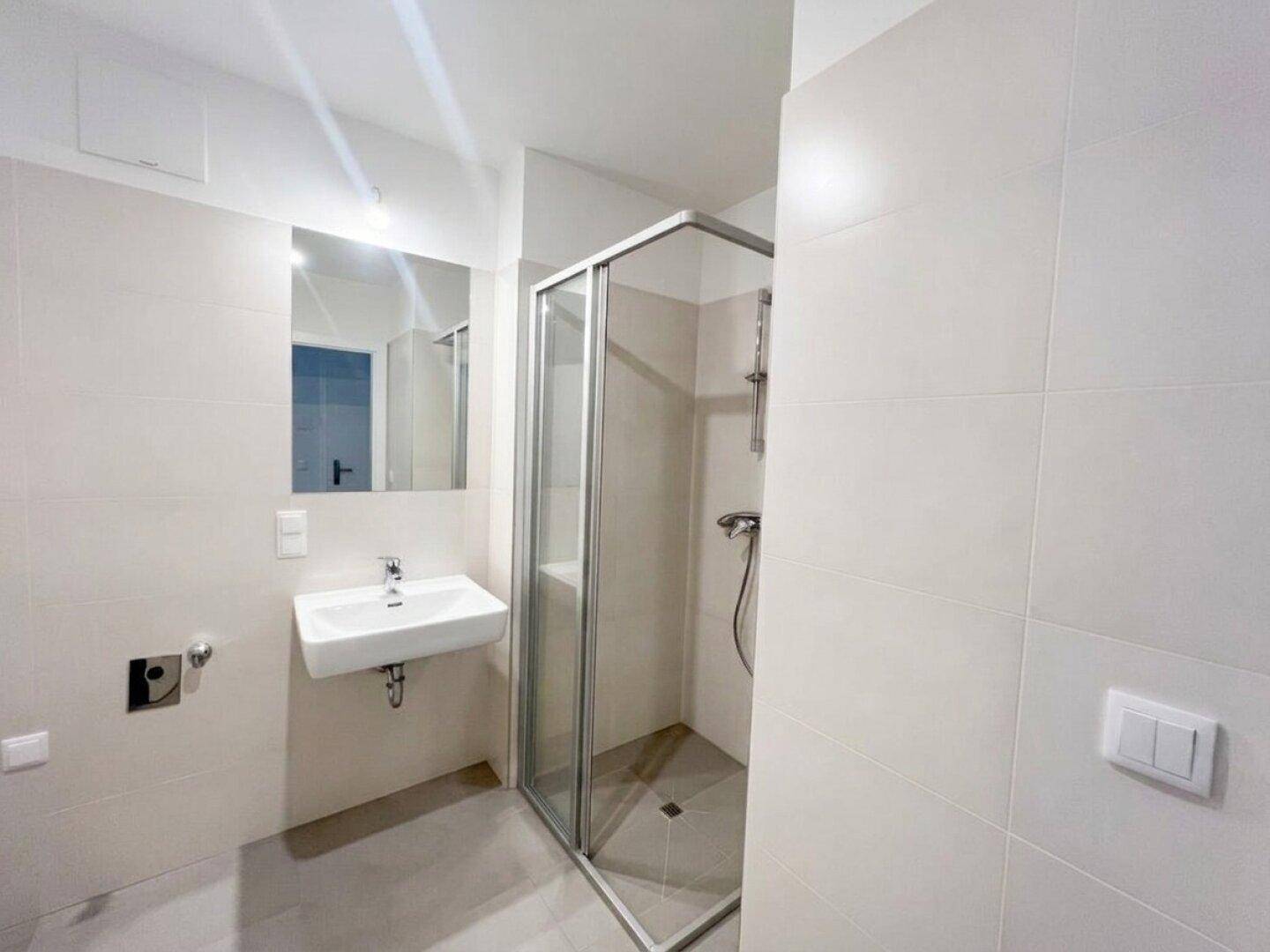 Modernes Badezimmer mit Duschkabine, Waschbecken und Spiegel, in hellen Fliesen gehalten.