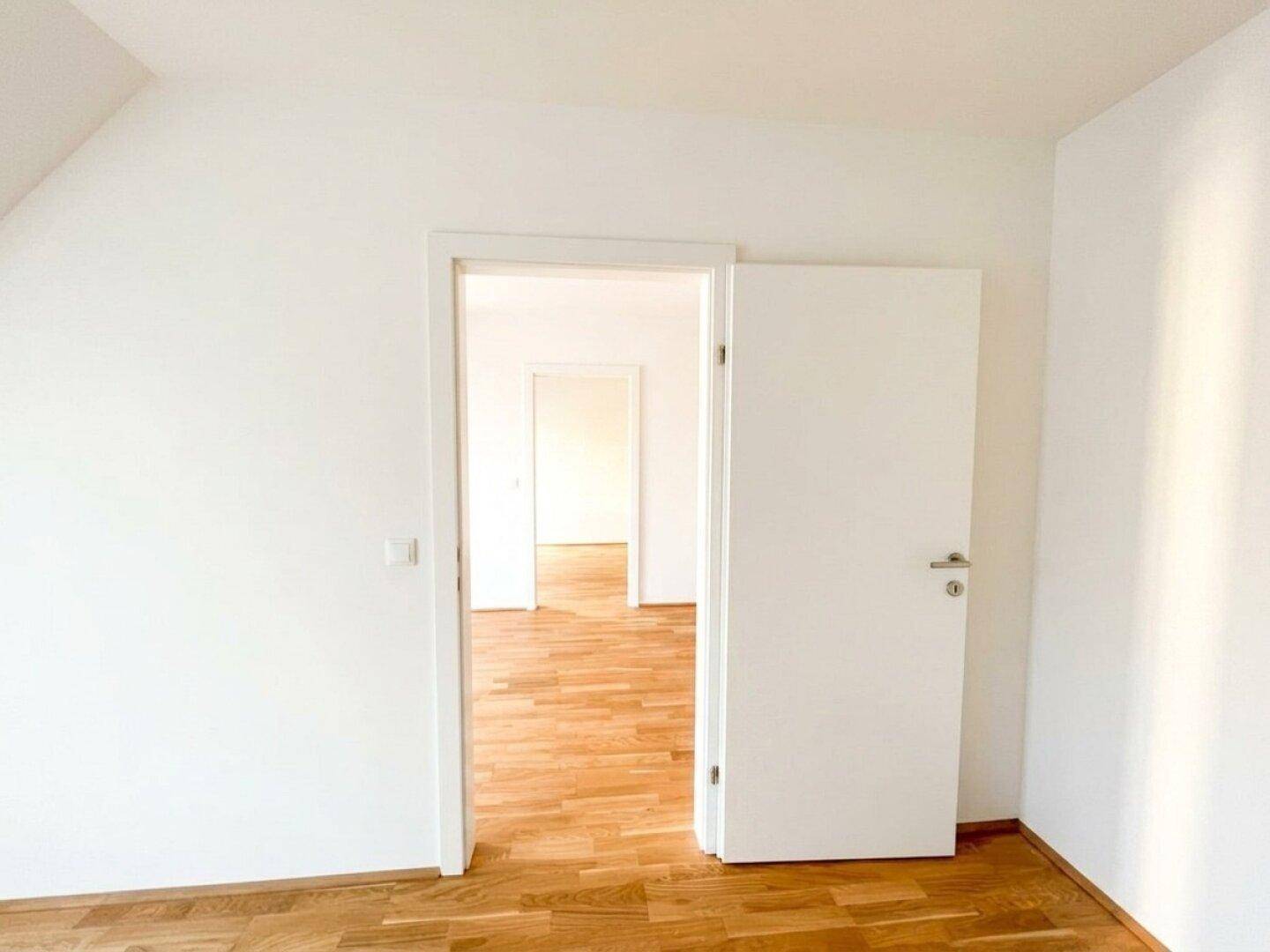 Heller, leerer Raum mit Holzboden und weiß gestrichenen Wänden, der vielseitig nutzbar ist.