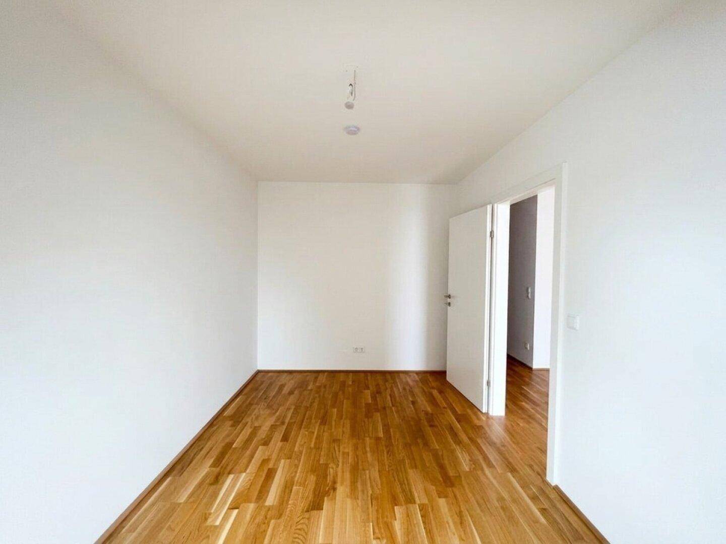 Heller, leerer Raum mit Holzboden und weißen Wänden, der vielseitig als Schlaf- oder Arbeitszimmer dienen kann.