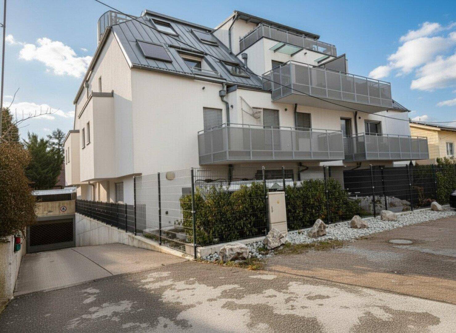 Seitenansicht des Wohnhauses mit Zufahrt zur Tiefgarage und modernen Balkonen.
