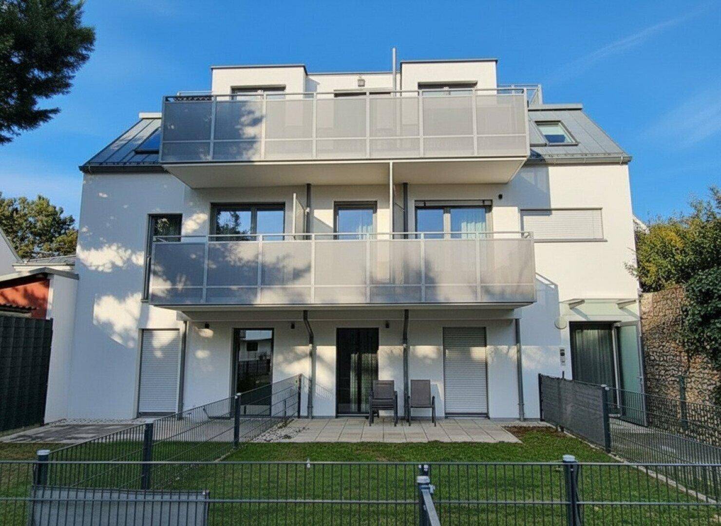 Rückansicht des modernen Wohnhauses mit Terrassen im Erdgeschoss und Balkonen in den oberen Etagen.