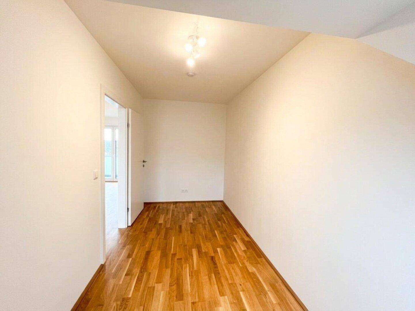 Leerer Raum mit Holzboden, weißen Wänden und einer leichten Dachschräge, ideal für ein Schlafzimmer.