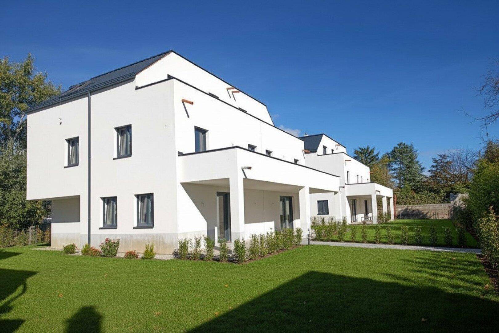 Moderne Reihenhäuser mit frisch angelegtem Rasen und klarem blauen Himmel.