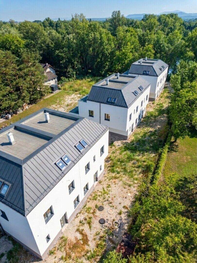 Reihenhäuser in moderner Architektur, umgeben von viel Grün und mit Wasserblick in der Ferne.