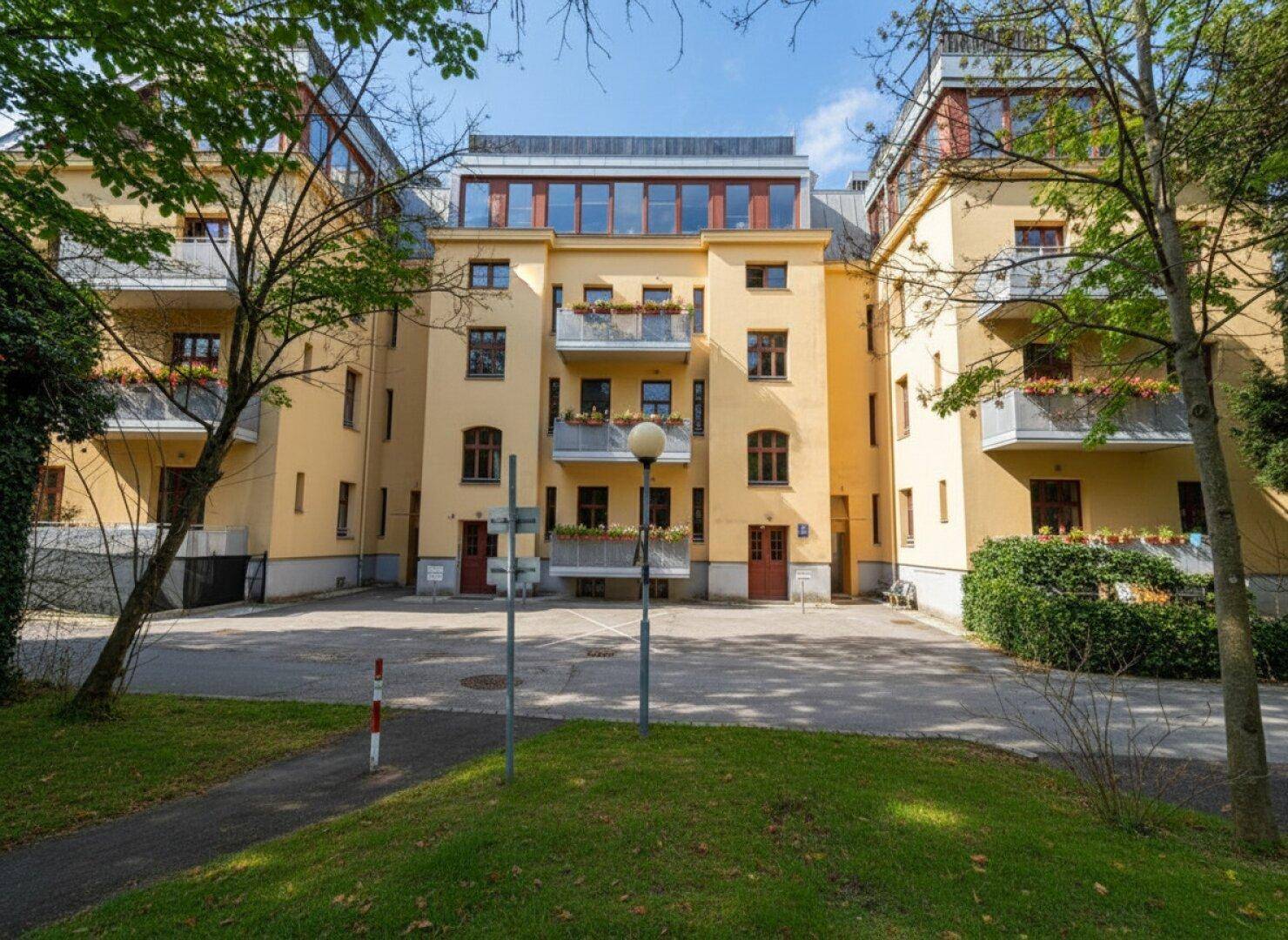 Gelbe Wohnanlage mit mehreren Balkonen und grüner Umgebung, umgeben von Bäumen und einem Innenhof.