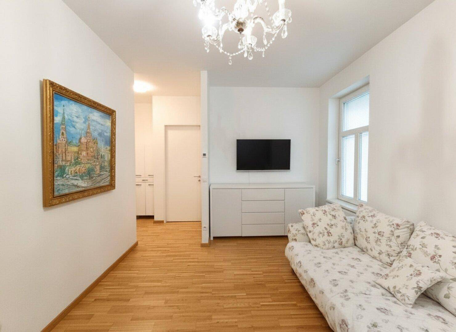 Gemütlicher Wohnbereich mit Sofa, Fernseher und Zugang zu einem hellen Flur mit Holzboden.