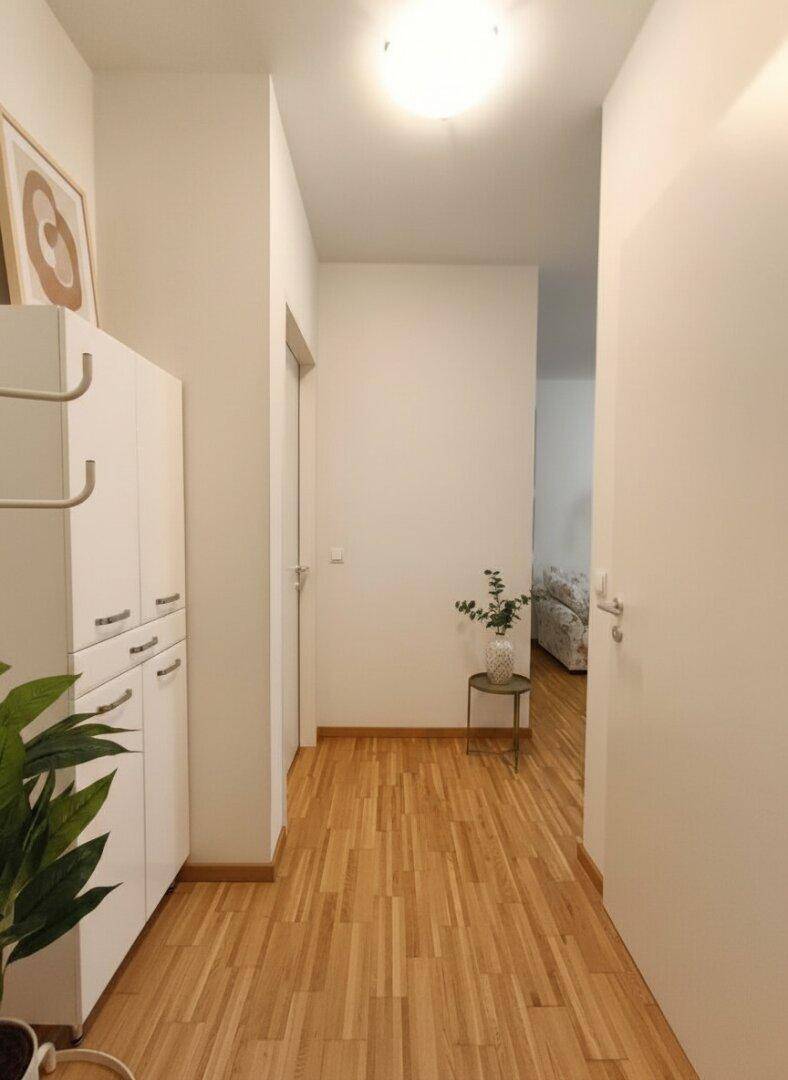Heller Flur mit Holzboden und weißen Wänden, der zu den verschiedenen Räumen der Wohnung führt.