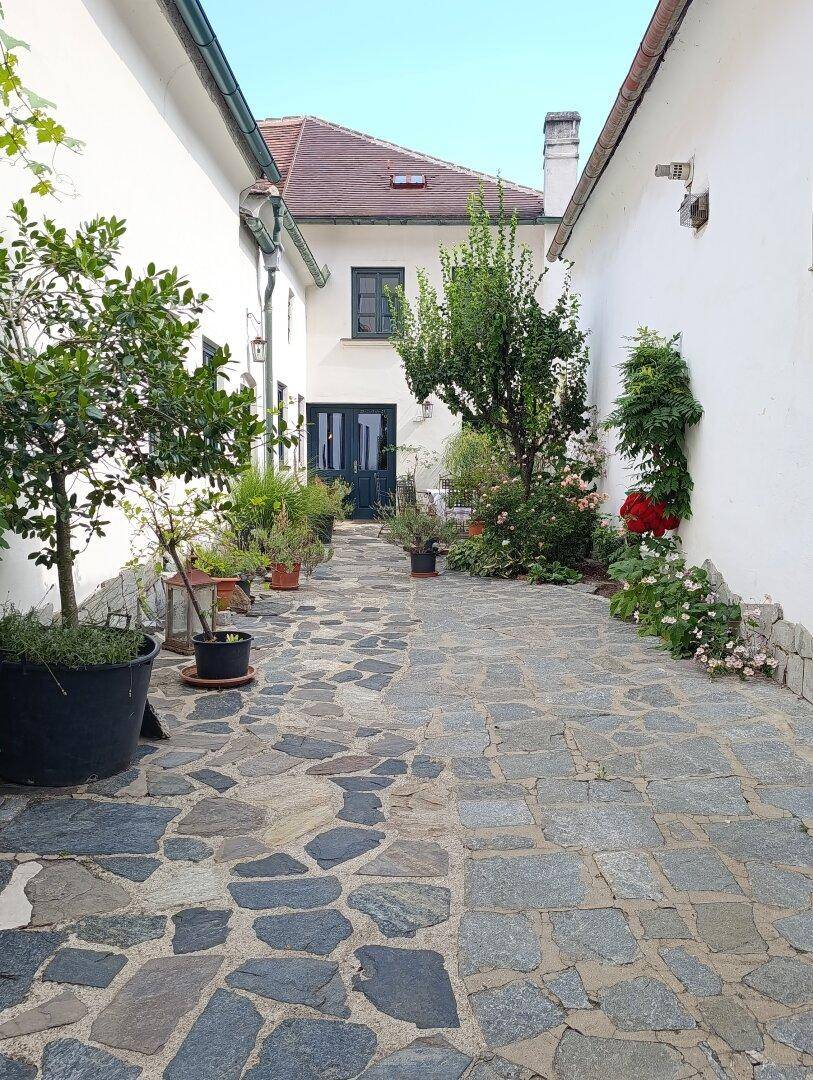 Historischer Innenhof mit Natursteinpflaster, vielen Topfpflanzen und weiß getünchten Fassaden.